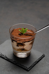 Portion of Classic tiramisu dessert in a glass cup on dark concrete background