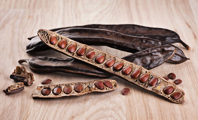 Carob pods and bean on wooden background.