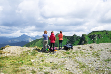 three unrecognizable girls on the edge of mountain looking on the green alps landscape