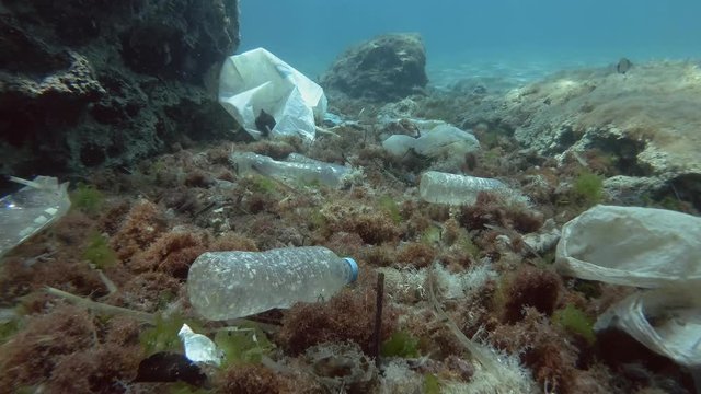  Plastic pollution, Tropical fishes swims over the bottom covered with a lot of plastic garbage. Slow motion. Plastic bottles, bags and dishes on the seabed in Mediterranean Sea, Europe. 