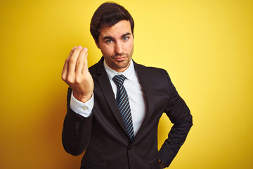 Young handsome businessman wearing suit and tie standing over isolated yellow background Doing Italian gesture with hand and fingers confident expression