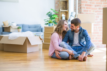 Young beautiful couple in love sitting on the floor together with cardboard boxes around for moving to a new house