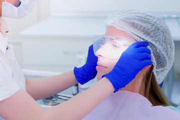 Dentist in gloves puts protective glasses on patient woman before teeth cure in dentistry. Young woman visit stomatologist. Teeth treatment in stomatology clinic. Protective equipment in medicine.