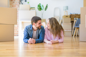 Fototapeta premium Young beautiful couple in love relaxing lying on the floor together with cardboard boxes around for moving to a new house