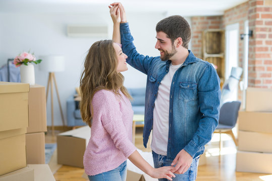 Young couple dancing celebrating moving to new apartment around cardboard boxes