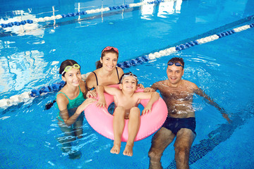 A happy family swims in a swimming pool indoors.