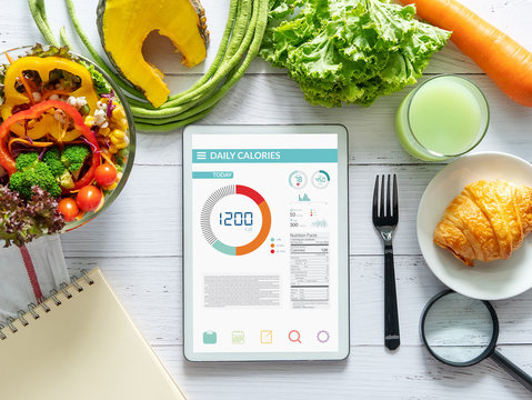 Calories counting , diet , food control and weight loss concept. tablet with Calorie counter application on screen at dining table with salad, fruit juice, bread and vegetable