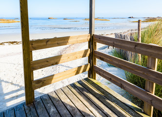View from a wooden porch over an empty sandy beach at low tide on a sunny morning in Penvenan, Brittany.