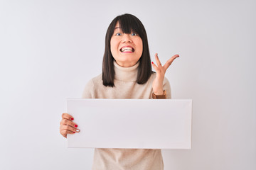 Young beautiful Chinese woman holding banner standing over isolated white background very happy and excited, winner expression celebrating victory screaming with big smile and raised hands