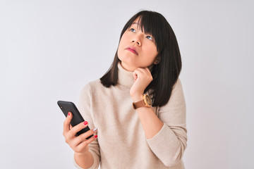 Young beautiful Chinese woman using smartphone standing over isolated white background serious face...