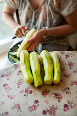  Four peeled courgettes on the table. In the background, the hands of the hostess peeling the courgettes.