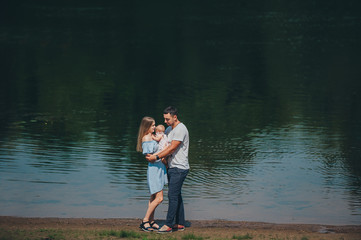 Parents with a baby daughter stand in the water on the lake shore and embrace.