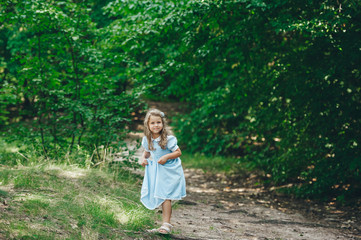 Smiling little girl in blue dress is standing on a forest path