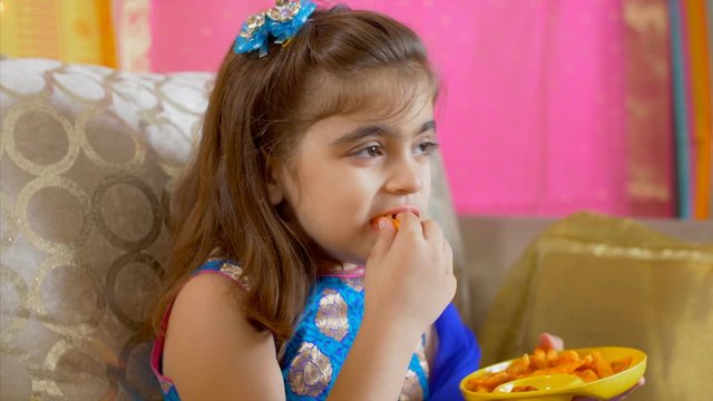 Slow motion shot of a little Indian girl eating fries in yellow plate. 
