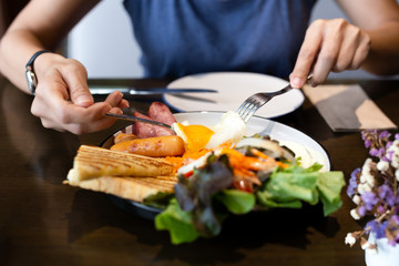 Woman having breakfast with fried eggs, sausages, vegetable salad and toast at cafe in the morning.