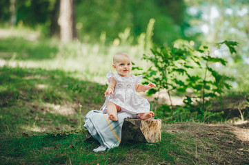 Toddler little girl sits on a stump in summer forest.