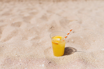 Glass of refreshing lemonade with a tube on a sand beach. Trip and summer relax concept. Copy space.