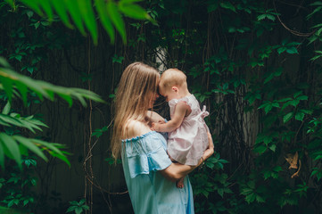 Mother is standing on the path in forest holding her baby girl daughter on her hands hugging and kissing her