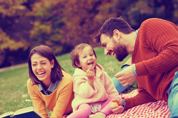 Happy little girl on picnic with her parents blowing dandelions