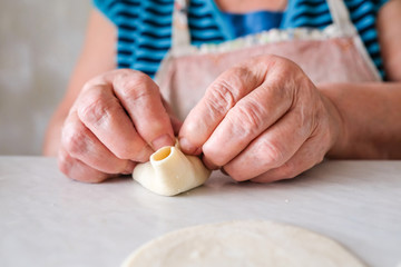 Old woman sculpts pasta. Grandma makes manti. Recipe for meat and dough.