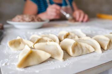 Fototapeta na wymiar Ready manti, dumplings at the grandmother's kitchen. An old woman is preparing a dish of dough.