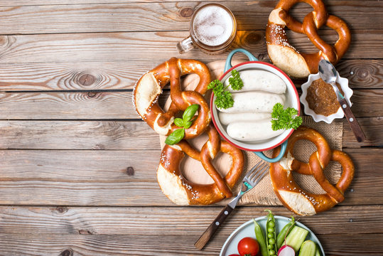 Pretzels, white bavarian sausages and vegetables on wooden background, german traditional food, oktoberfest