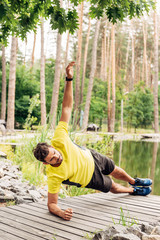 Obraz premium Athletic man in sportswear doing exercise near lake in forest