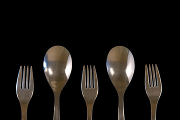 metal forks and spoons on a black background. top view on stainless spoons and forks with copy space