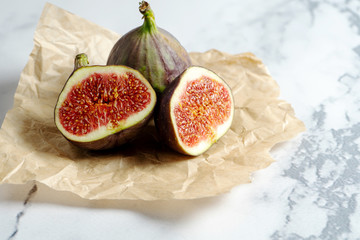 Close up view on Fresh figs. Exotic fruit. Sliced fig on craft paper on marble background. Copy...