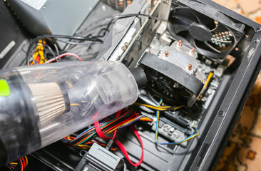 Inside details of the personal computer. Man is cleaning wires with vacuum cleaner. Small hoover. Motherboard and video card in the dust. Broken PC.
