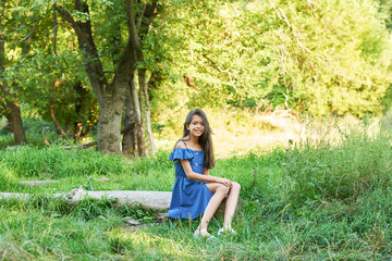 teenager girl in a blue dress walks in the summer forest at sunset