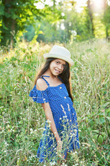 girl in a blue dress and hat walks in a field in the summer at sunset