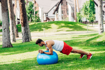 bearded man in sportswear exercising on blue fitness ball in park