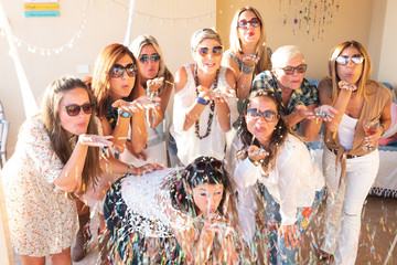 a group of nine beautiful women blows on confetti celebrating the party or a birthday. Positive...
