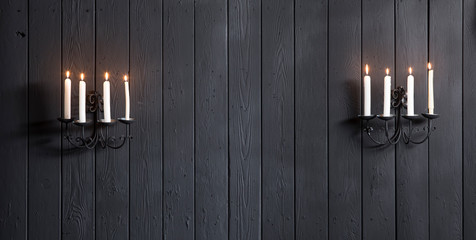 vintage wall candlesticks with candles on a black wooden wall