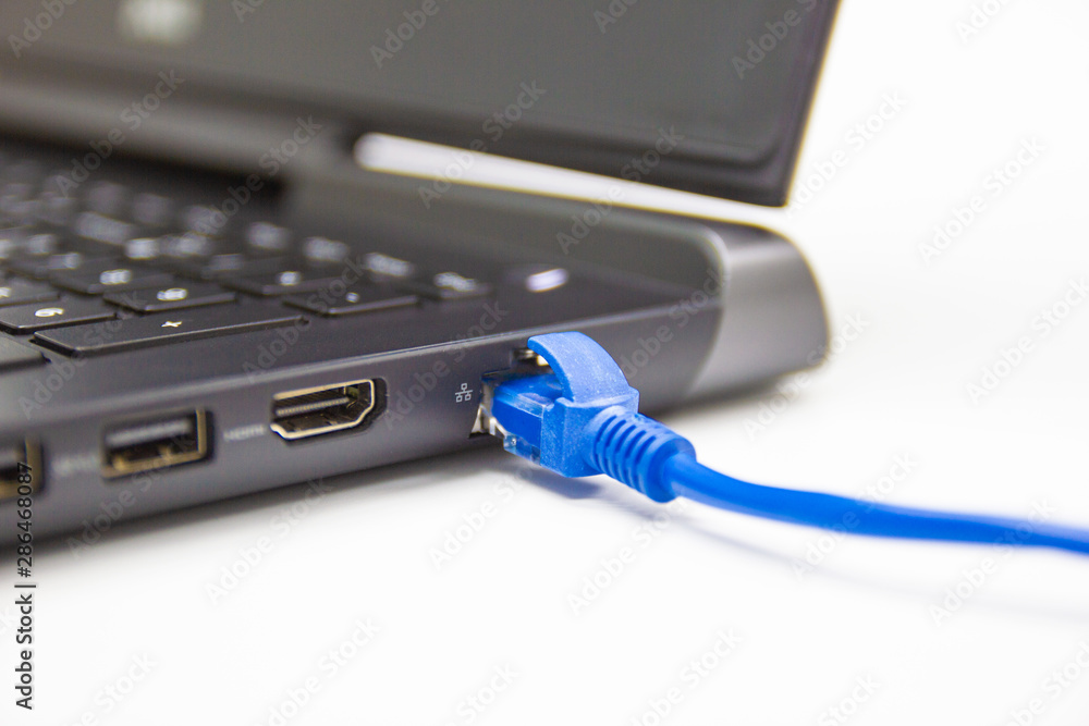 Poster closeup blue cable network connection to a lan port of laptop computer on white table, concept compu