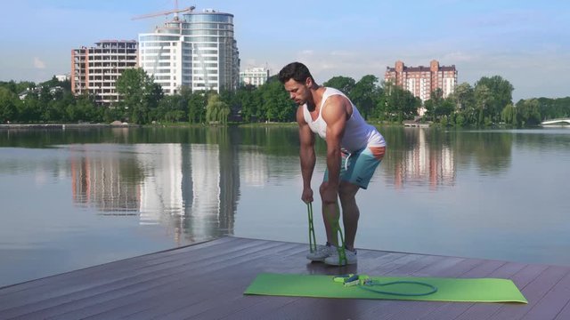Athletic and muscular man stretching rubber band near lake