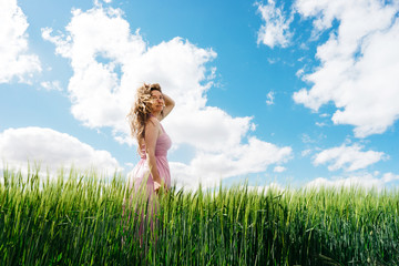 Long-haired woman in a pink dress on a field of green wheat. The concept of freedom and freshness. Beautiful wheat, great design for any purposes. Female symbol. Agriculture harvest