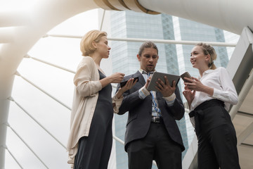 caucasian businesspeople standing and having business talking with hands holding tablet and smartphone in city