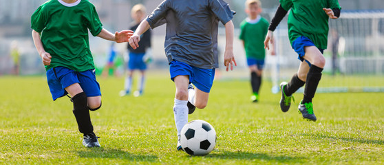 Plakat Boy Kicking Soccer Ball. Running Soccer Football Players. Five Junior Footballers on Duel. Football Grass Field and Soccer Stadium in the Background.