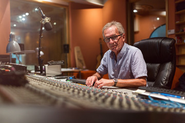 Male middle aged recording engineer in a recording studio sitting at a multi channel console