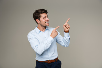 Image of cheerful smiling man wearing formal clothes looking and pointing finger aside at copyspace