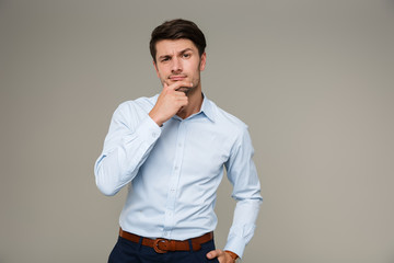 Image of thinking serious man wearing formal clothes looking at camera and touching his chin