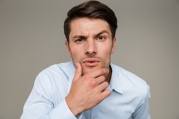Image closeup of brooding serious man wearing formal clothes looking at camera and touching his chin