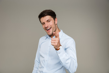 Image of cheerful unshaven man wearing formal clothes smiling and pointing finger at camera while winking