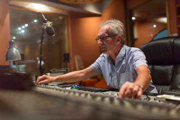 Male middle aged recording engineer in a recording studio sitting at a multi channel console