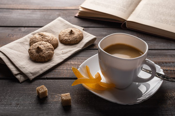Cup of black coffee with candied oranges and lumps of sugar. Ccookies on a linen napkin and an open book