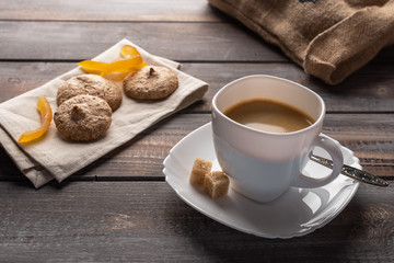A cup of black coffee with candied oranges and lumps of sugar. Biscuits on a linen napkin and a bag of coffee