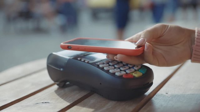 Customer paying for order in the cafe with payment terminal using NFC smartphone technology girl applying mobile phone on cash machine device digital e-money e-wallet electronic close up slow motion