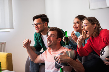 Group of cheerful friends watching soccer match at home and celebrating victory.